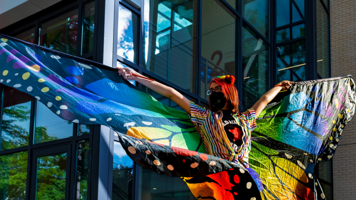 Performer spreading constructed butterfly wings outside the Madison Youth Arts center