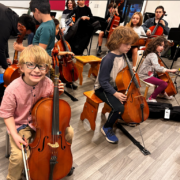 Multiple young children playing cellos in a classroom